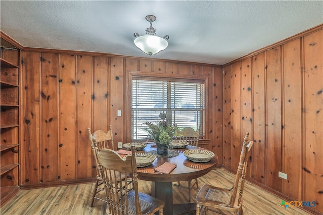 dining area featuring wooden walls, a textured ceiling, crown molding, and light hardwood / wood-style flooring