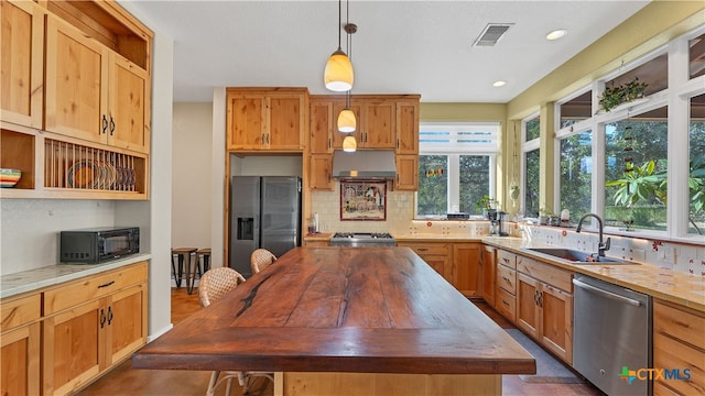 kitchen with a center island, sink, backsplash, appliances with stainless steel finishes, and decorative light fixtures