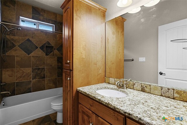 full bathroom with vanity, a textured ceiling, toilet, and tiled shower / bath