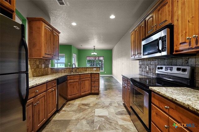 kitchen featuring sink, light stone counters, appliances with stainless steel finishes, a textured ceiling, and decorative light fixtures