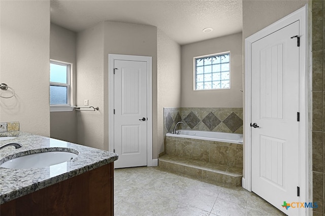 bathroom with tile patterned flooring, vanity, a textured ceiling, and a relaxing tiled tub