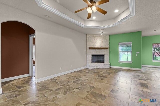 unfurnished living room featuring a fireplace, ceiling fan, a textured ceiling, and a raised ceiling