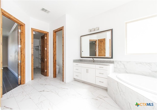 bathroom with vanity, tiled tub, and toilet