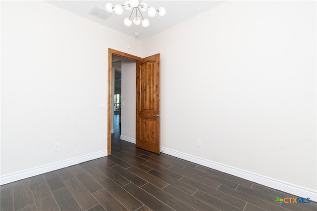 empty room with dark wood-type flooring and a chandelier