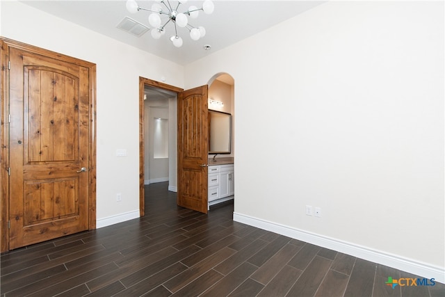 unfurnished bedroom with ensuite bathroom, dark hardwood / wood-style floors, and a notable chandelier