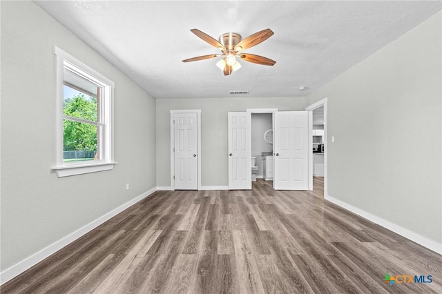 unfurnished bedroom with ceiling fan, a textured ceiling, baseboards, wood finished floors, and visible vents