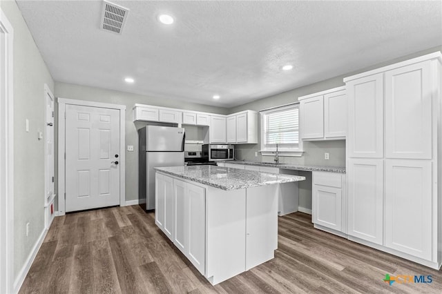 kitchen with visible vents, a kitchen island, white cabinetry, dark wood finished floors, and stainless steel appliances