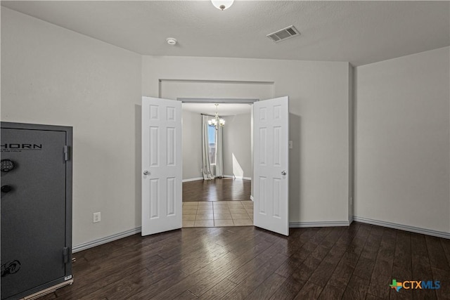 empty room with baseboards, hardwood / wood-style floors, a notable chandelier, and visible vents