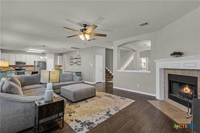 living room featuring a ceiling fan, visible vents, stairs, a tile fireplace, and baseboards