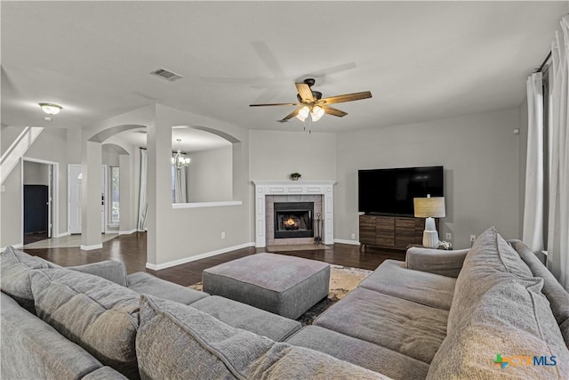living area featuring visible vents, baseboards, arched walkways, ceiling fan with notable chandelier, and a tile fireplace