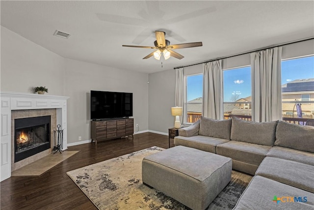 living room with ceiling fan, dark wood-type flooring, visible vents, a tile fireplace, and baseboards