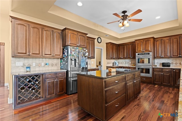 kitchen featuring stainless steel appliances, a tray ceiling, a center island, dark wood-type flooring, and recessed lighting