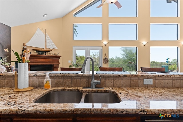 kitchen with a sink, light stone counters, a ceiling fan, a towering ceiling, and open floor plan