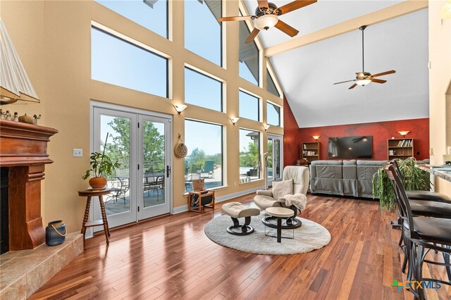 living area featuring a ceiling fan, a high ceiling, wood finished floors, beamed ceiling, and a high end fireplace
