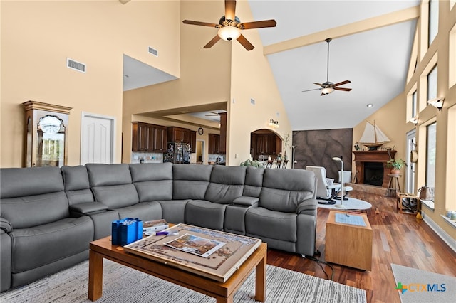 living room featuring a ceiling fan, high vaulted ceiling, a fireplace with raised hearth, and wood finished floors