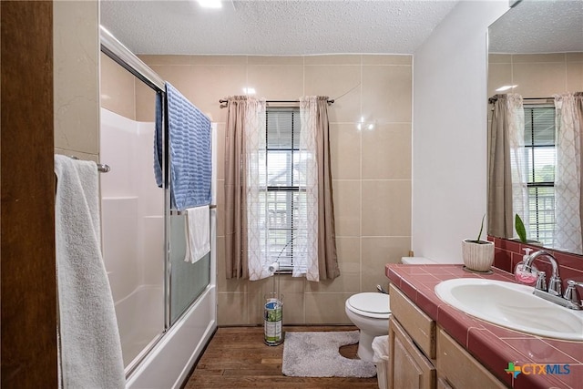 bathroom featuring wood finished floors, toilet, vanity, a textured ceiling, and tile walls