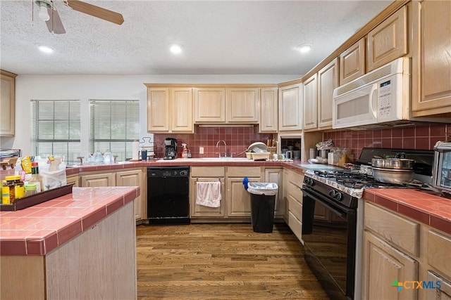 kitchen featuring black appliances, tile counters, a sink, wood finished floors, and backsplash