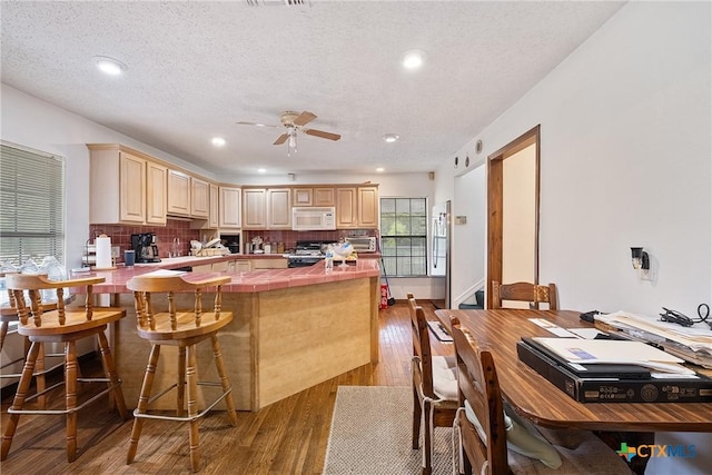 kitchen featuring white microwave, gas range, tile counters, wood finished floors, and ceiling fan