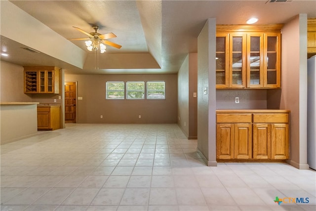 kitchen with a tray ceiling, a textured ceiling, light tile patterned floors, and ceiling fan