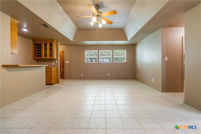 unfurnished living room featuring light tile patterned flooring, bar, ceiling fan, and a raised ceiling