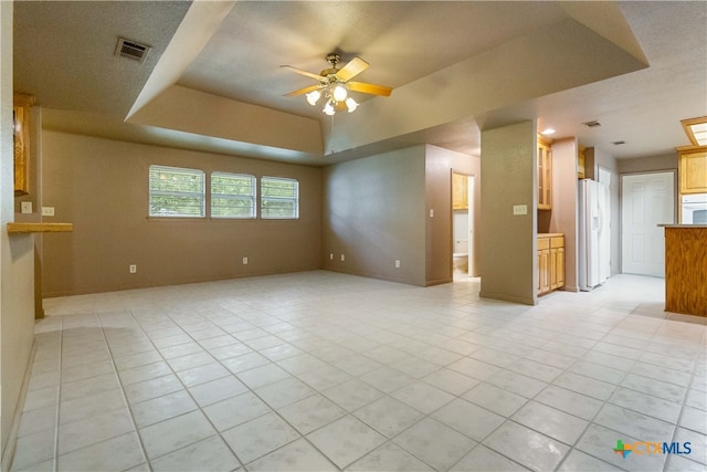 unfurnished living room with a textured ceiling, a raised ceiling, light tile patterned floors, and ceiling fan