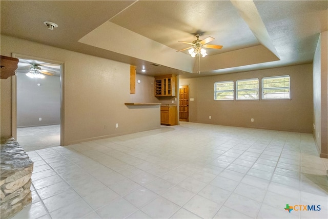 unfurnished living room with ceiling fan, a raised ceiling, and light tile patterned floors