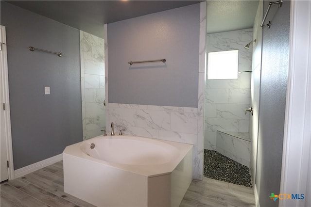 bathroom with wood finished floors, baseboards, a bath, and a walk in shower