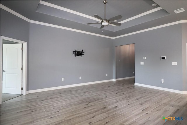 empty room featuring visible vents, a tray ceiling, wood finished floors, and ornamental molding