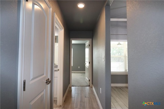 hall featuring a textured wall, baseboards, and wood finish floors