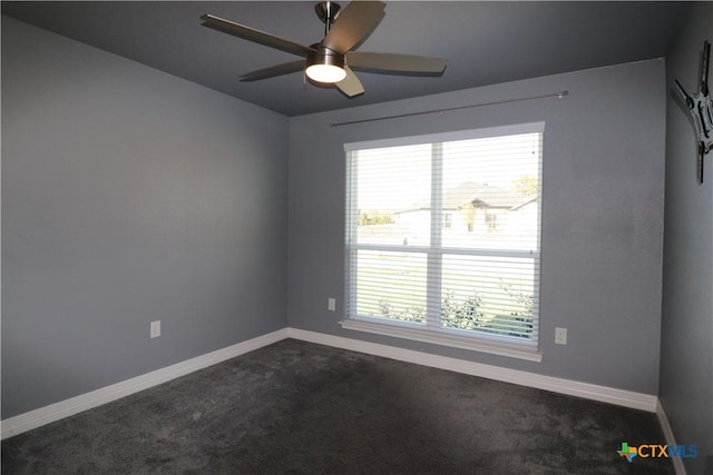 empty room with dark colored carpet, a ceiling fan, and baseboards