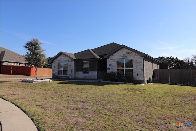 view of front facade with stone siding, a front yard, and fence