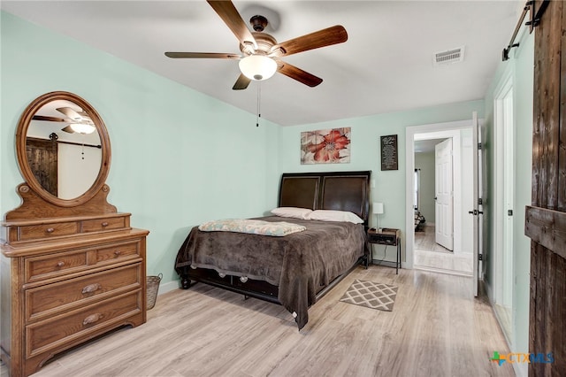 bedroom featuring a barn door, light hardwood / wood-style flooring, and ceiling fan