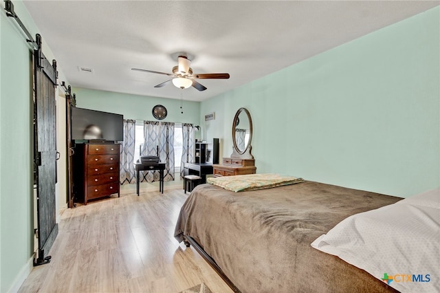 bedroom featuring a barn door, ceiling fan, and light hardwood / wood-style floors