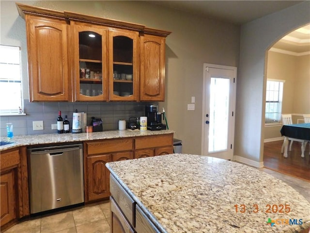 kitchen featuring backsplash, glass insert cabinets, dishwasher, brown cabinets, and arched walkways