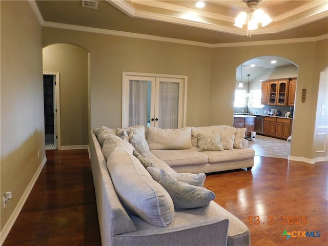 living room featuring a tray ceiling, french doors, arched walkways, and wood finished floors