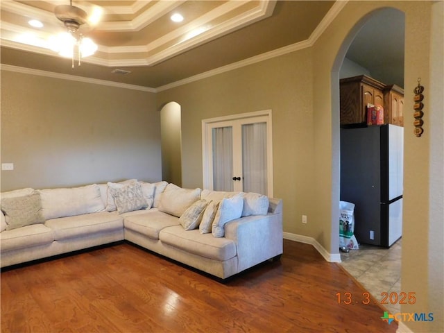 living room featuring light wood-type flooring, a tray ceiling, ornamental molding, arched walkways, and a ceiling fan