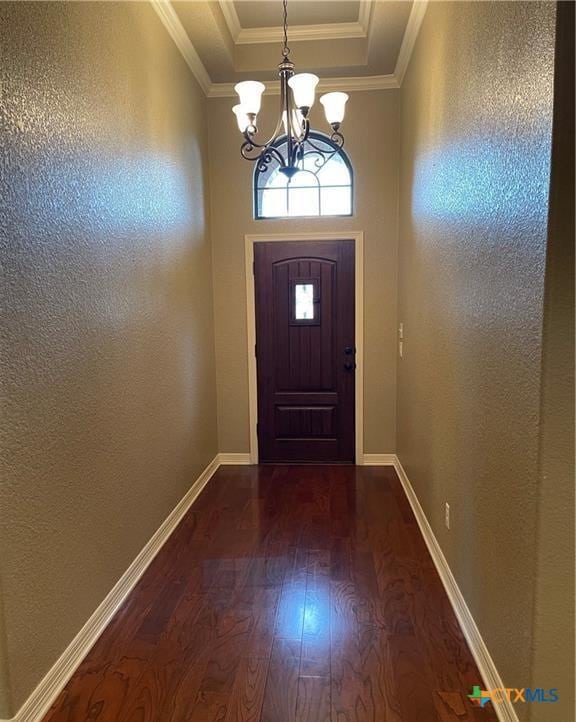 entryway featuring dark wood-type flooring, ornamental molding, a tray ceiling, an inviting chandelier, and baseboards