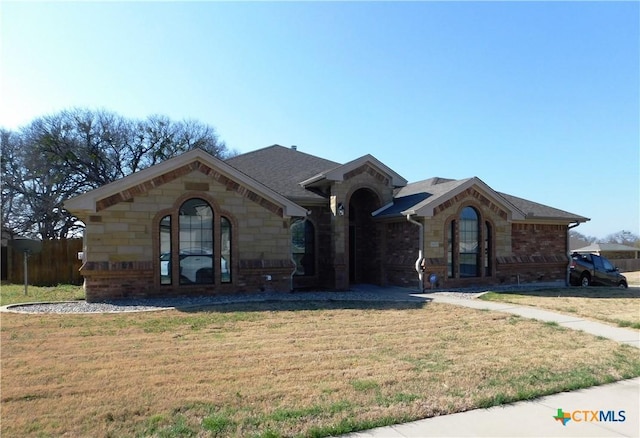 view of front of home with a front lawn, stone siding, and roof with shingles