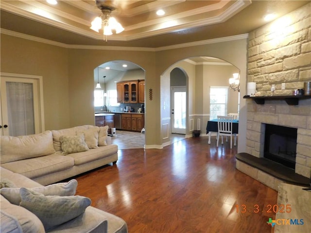 living area with a tray ceiling, arched walkways, and dark wood finished floors