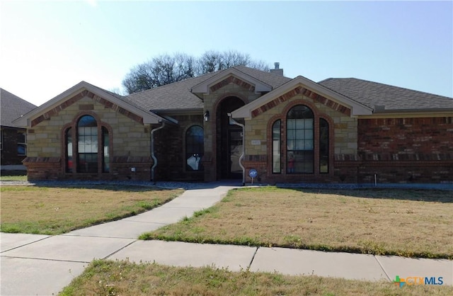 view of front facade featuring stone siding, roof with shingles, and a front lawn