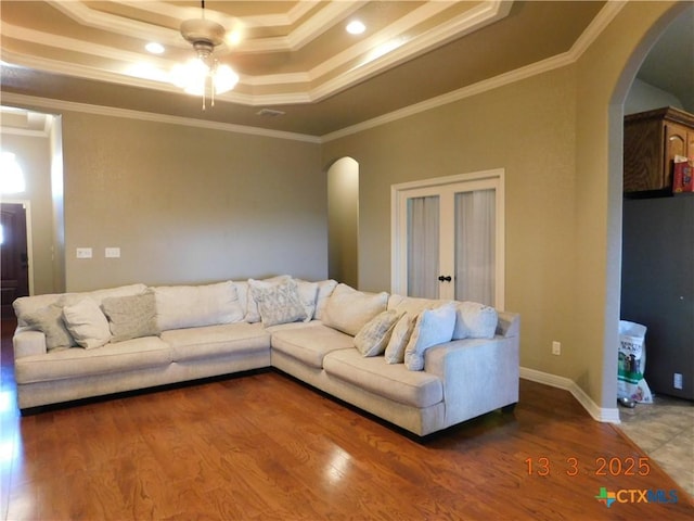 living room featuring arched walkways, a raised ceiling, and wood finished floors