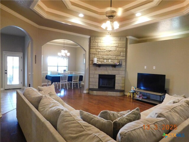 living room featuring wood finished floors, arched walkways, a raised ceiling, and a chandelier