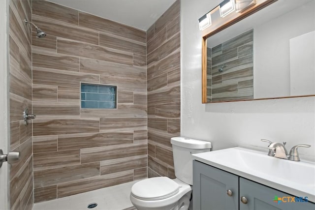 bathroom featuring vanity, a tile shower, and toilet