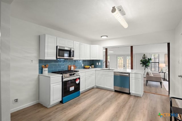 kitchen featuring appliances with stainless steel finishes, white cabinetry, sink, backsplash, and light hardwood / wood-style flooring