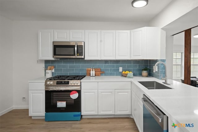 kitchen featuring sink, light hardwood / wood-style flooring, stainless steel appliances, decorative backsplash, and white cabinets