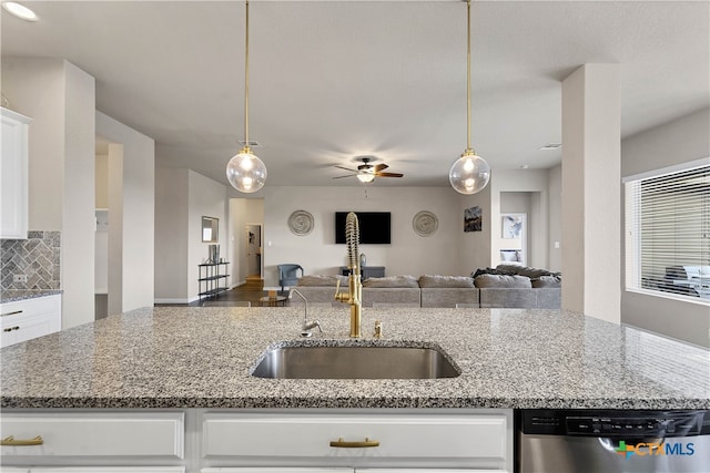kitchen featuring open floor plan, light stone countertops, decorative backsplash, stainless steel dishwasher, and a sink