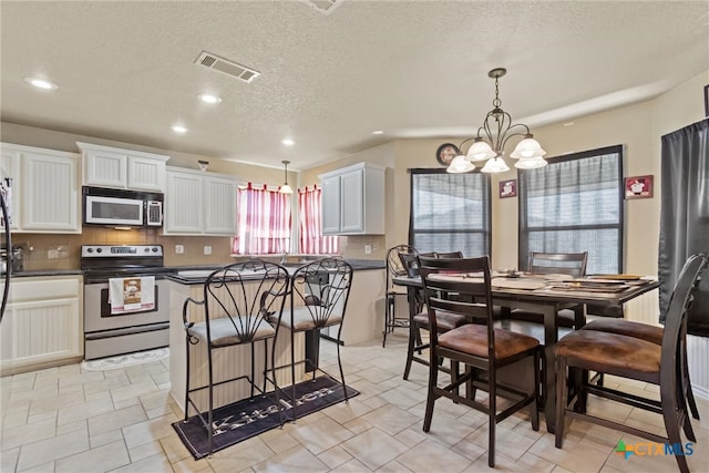 kitchen featuring backsplash, appliances with stainless steel finishes, decorative light fixtures, a notable chandelier, and white cabinets