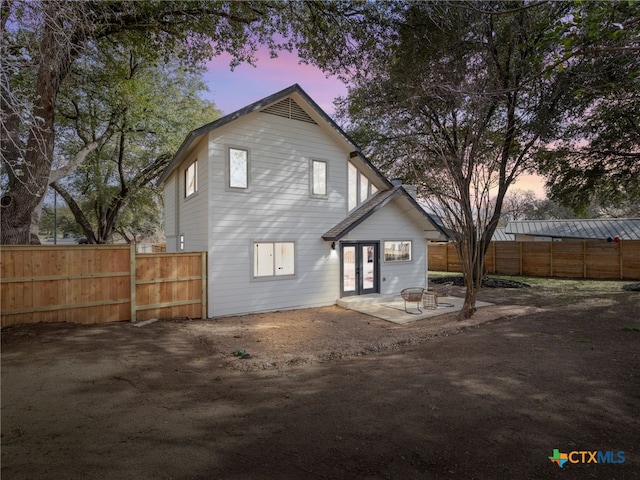 back of property at dusk with french doors, a patio area, and fence