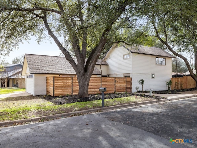 view of home's exterior with a shingled roof, brick siding, and fence