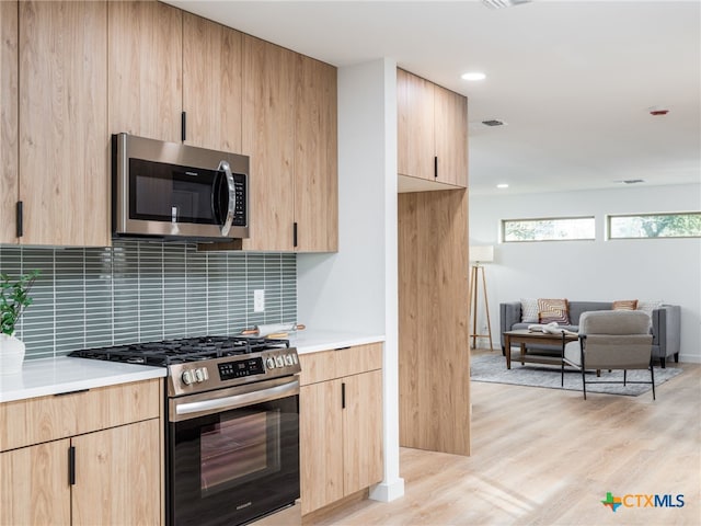 kitchen with backsplash, appliances with stainless steel finishes, open floor plan, light brown cabinets, and light wood-type flooring